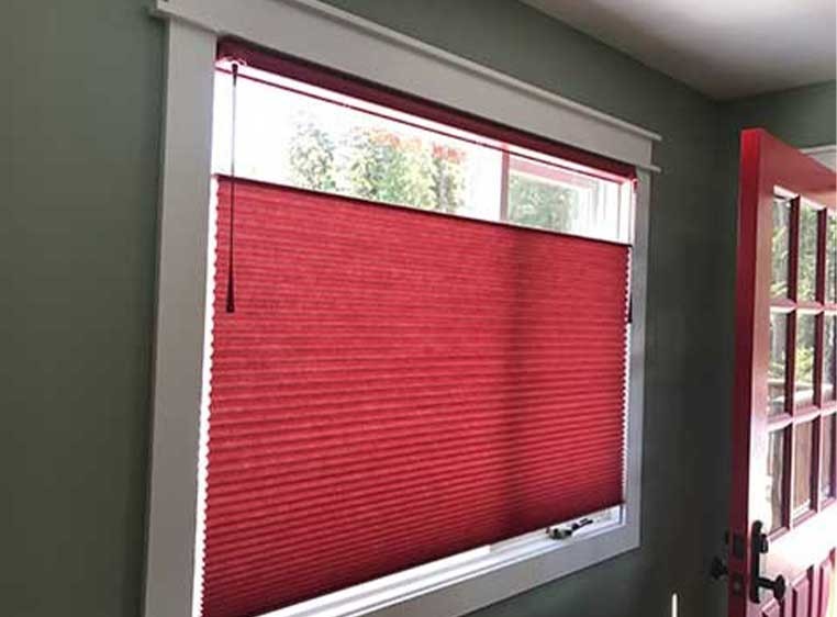 Red honeycomb shades on a square window